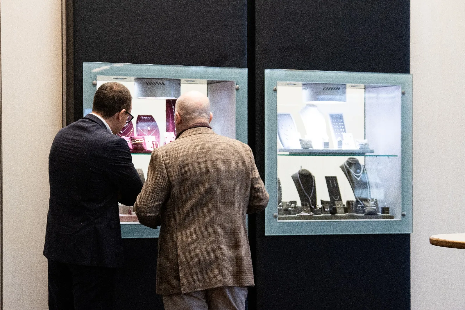 Two visitors looking at jewellery in illuminated showcases during the 2025 edition.