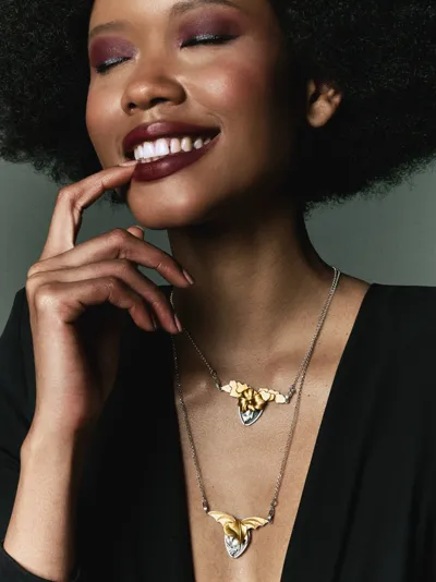 Smiling model wearing two necklaces with winged pendants in silver and bronze, Oneiroi collection