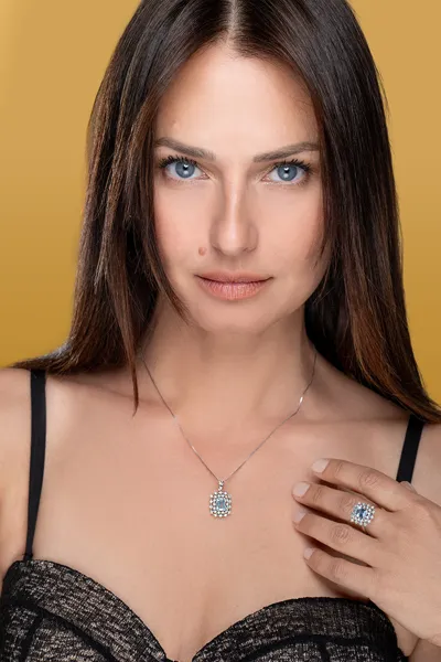 Model wearing a pendant and ring with a light blue gemstone and diamonds