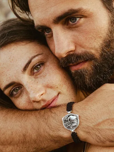 Couple embracing, the man wearing a cord bracelet with a silver micro-sculpture medallion, Panorami del cuore collection