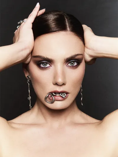 Model holding a silver snake ring between her lips, wearing long silver snake earrings and rings from the Aghatos collection