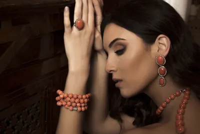 Model wearing coral cabochon earrings and ring with coral bead bracelets and necklace