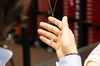 A hand holding up a fine necklace with a pendant in front of the display cases.