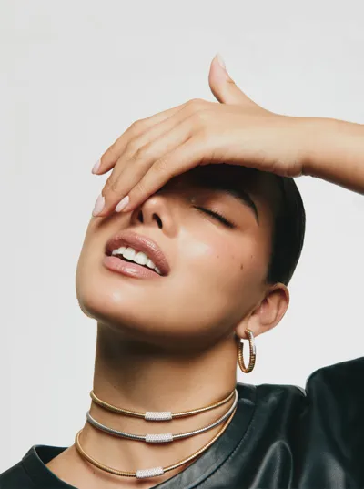 Model wearing three Tubogas chokers in yellow, white and rose gold with diamond bars, and a gold hoop earring