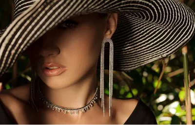 Model in a wide-brimmed hat wearing long diamond drop earrings and a diamond choker