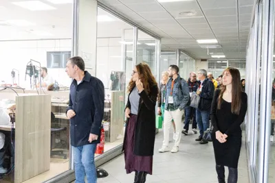 Participants walking along a corridor lined with glass-fronted workshops.