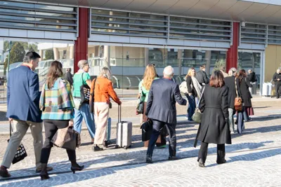 Participants arriving at the exhibition centre, walking towards the entrance with their luggage.