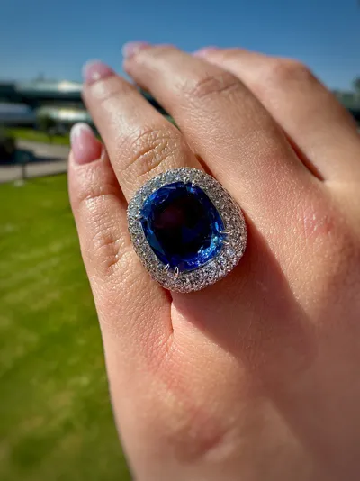 Hand wearing an 18Kt white gold ring with a 10 ct blue sapphire cushion and diamonds