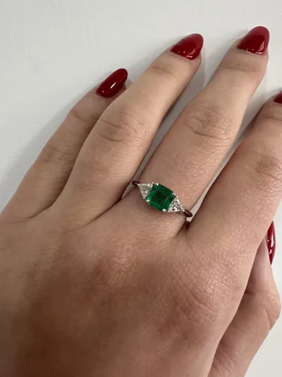 Hand wearing an 18Kt white gold ring with an emerald-cut emerald and two triangle diamonds