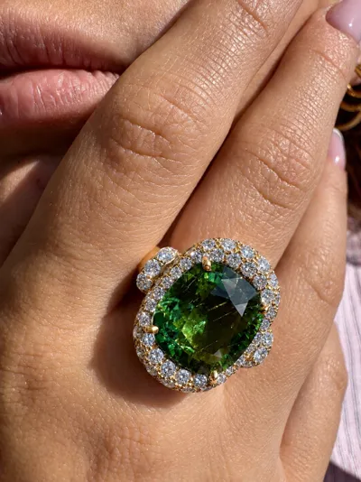 Hand wearing an 18Kt yellow gold ring with a green Paraiba cushion and diamonds