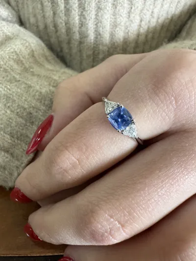 Hand wearing an 18Kt white gold ring with a blue sapphire cushion and two triangle diamonds