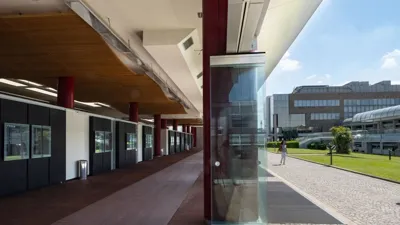 The covered walkway of Il Tarì Gold Centre: red columns, glass walls and pavilions beyond the lawn.