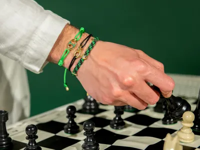 Hand wearing bracelets in gold and emeralds with marine cord, over a chessboard
