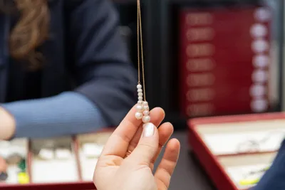 A hand holding a pearl pendant on a fine chain.