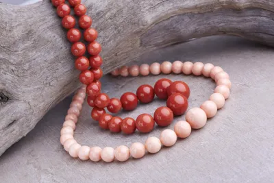Strands of red and pale pink coral beads on driftwood