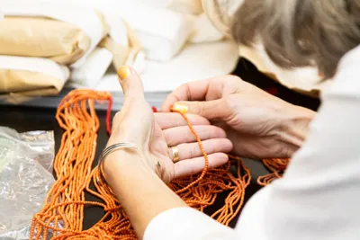 Hands sorting strands of orange coral beads.