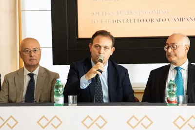 Three speakers at the conference table; the one in the centre speaks into a microphone.