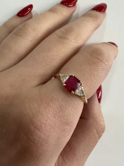 Hand wearing an 18Kt yellow gold ring with an emerald-cut ruby and two triangle diamonds