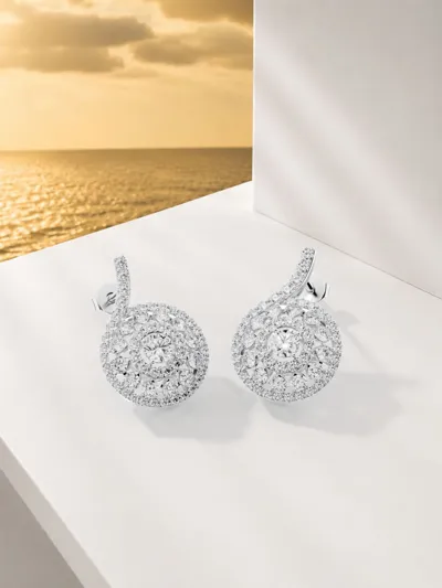 Round diamond earrings from the Snail collection on a white ledge by the sea
