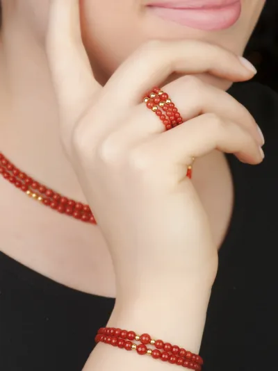 Model wearing a coral and yellow gold bracelet, necklace and rings, Classic line