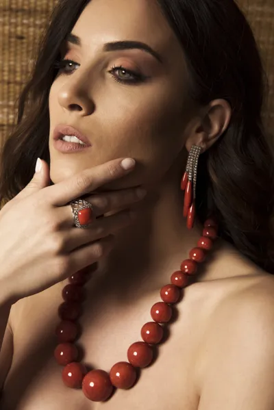 Model wearing a graduated red coral bead necklace, coral drop earrings and a coral ring